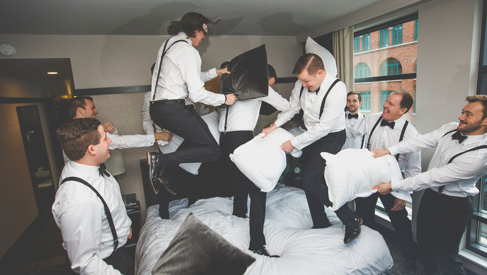 Groomsmen stage a pillow fight in the one bedroom suite